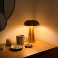 Morel brass mushroom table lamp lit on a wooden dressing table at night, beside a mug and a dish of rings