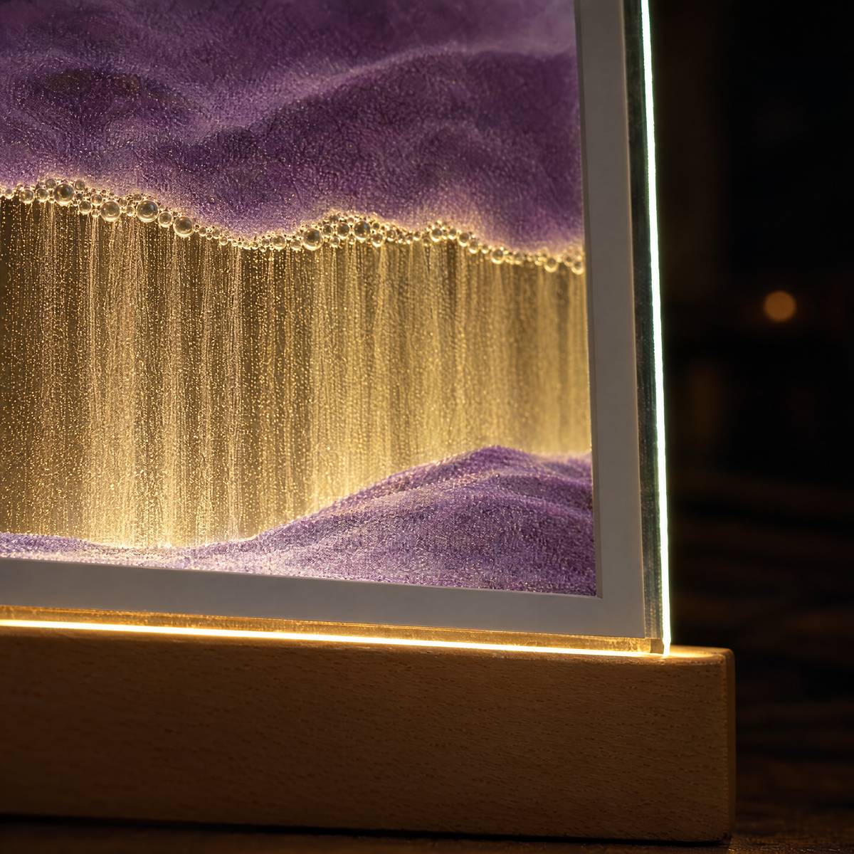 Close-up of purple sand, fine falling grains and the warm-lit glass edge