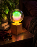 Aurora iridescent glass globe lamp glowing beside leafy plants and dark bedding