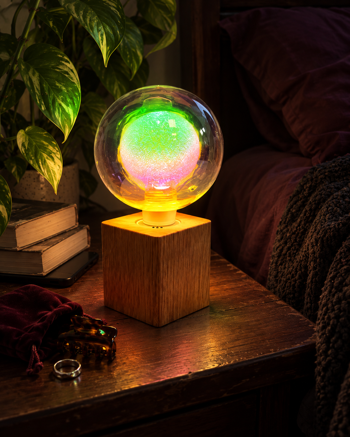 Aurora iridescent glass globe lamp glowing beside leafy plants and dark bedding