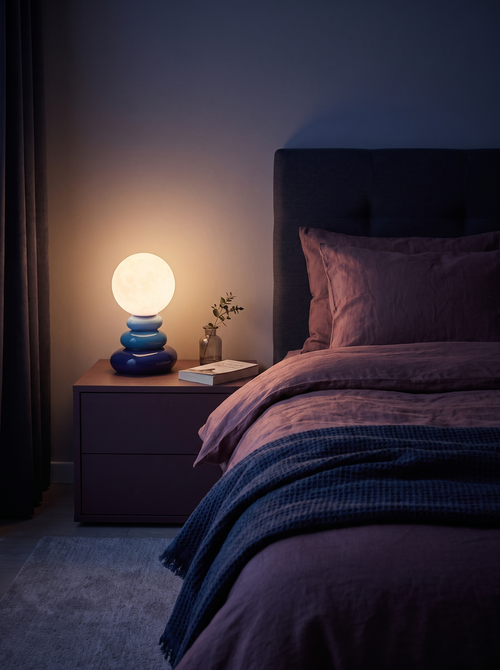 Cairn table lamp casting warm light across a dark bedroom with plum linen