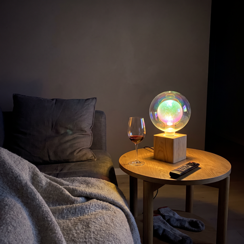 Aurora iridescent glass globe lamp lit on a side table beside a sofa at night