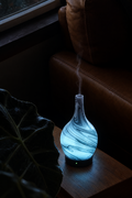 Nebula marbled glass diffuser glowing pale blue beside a leather armchair