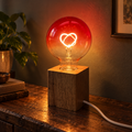 Red Ember heart-filament table lamp glowing on a wooden console at night