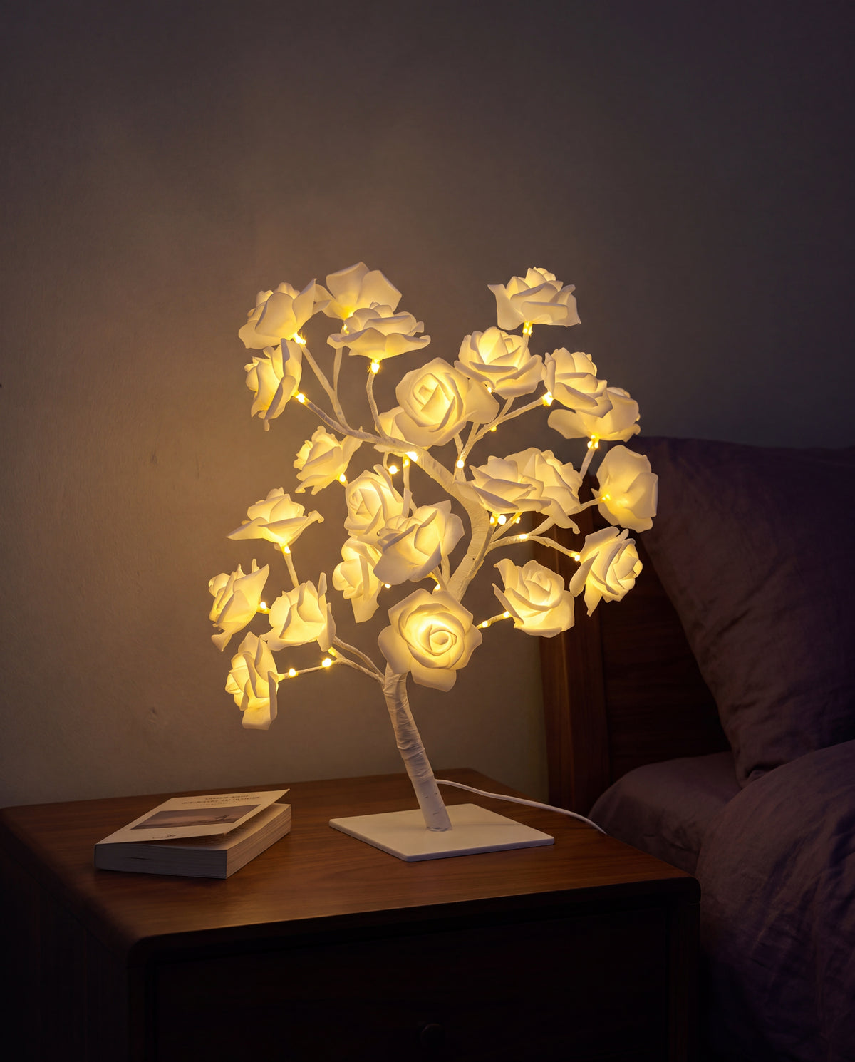 Cream-white Floreo rose tree lamp lit on a bedside table