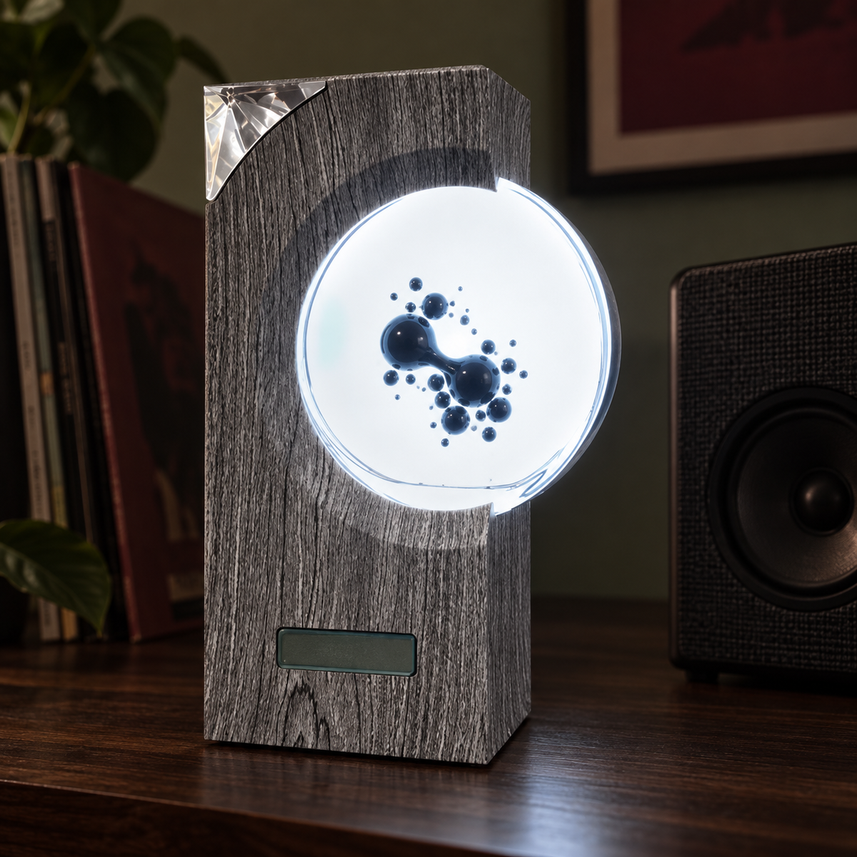 Fluxus gray ferrofluid display with glossy liquid forms and white backlighting beside a separate speaker