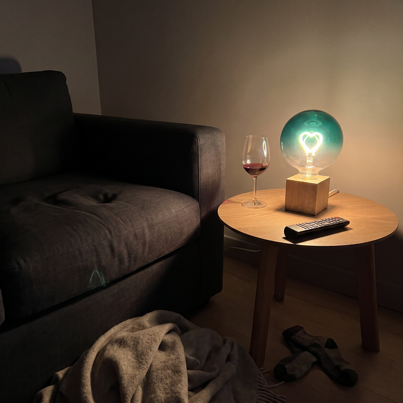 Ember heart filament table lamp in green, lit on a side table beside a sofa