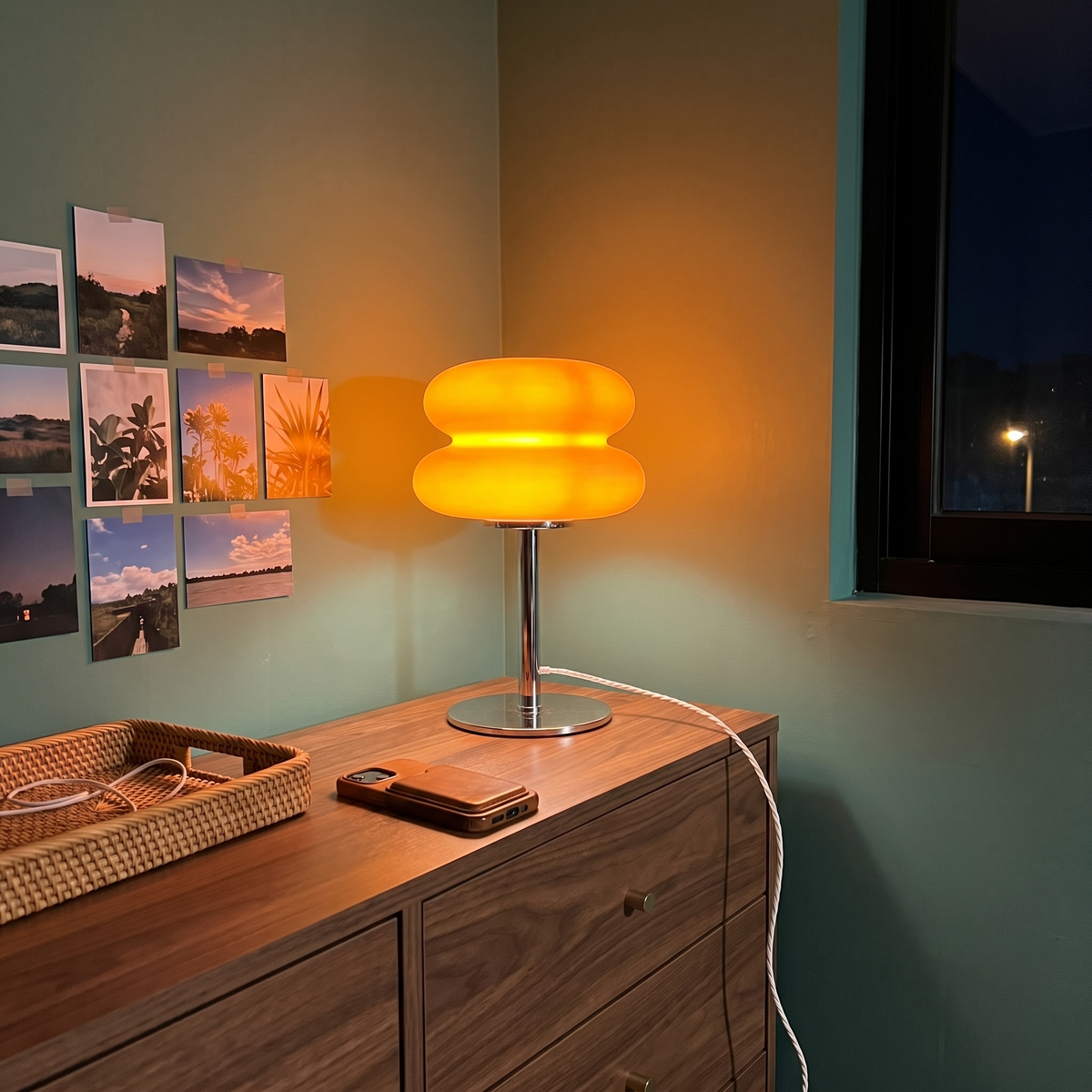 Orange Cumulus table lamp lit on a walnut chest of drawers at night