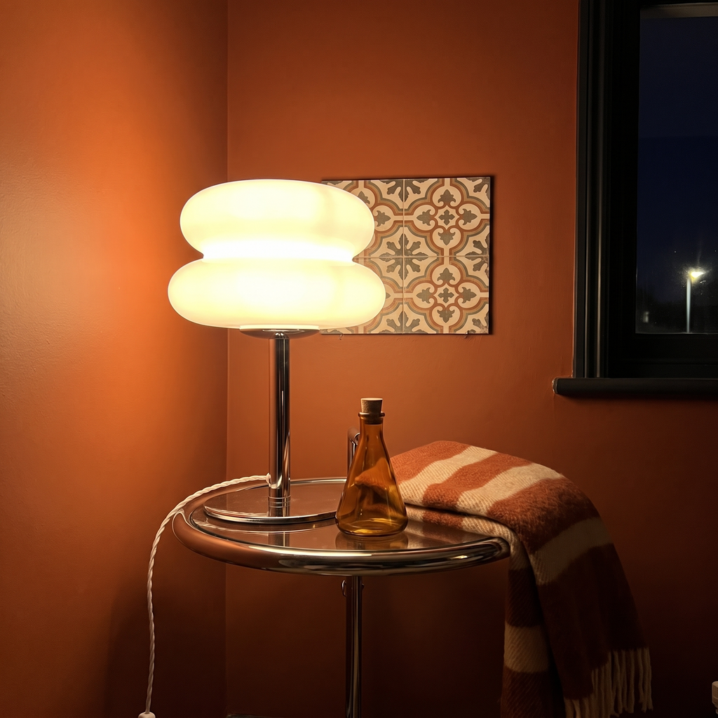 White Cumulus table lamp lit on a round side table against a terracotta wall