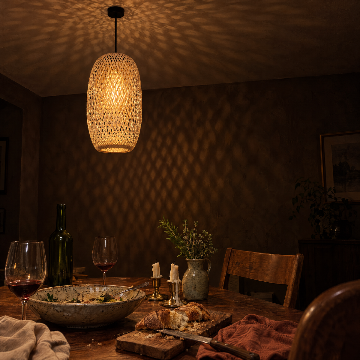 Tessera woven bamboo pendant hanging over a dining table after dinner, warm light through the bamboo weave