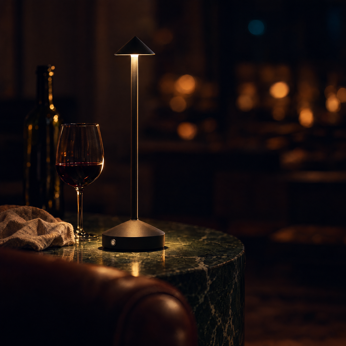 Spire table lamp in black, lit on a green marble side table beside a glass of red wine at night