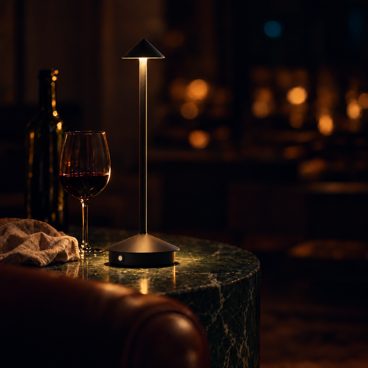 Black Spire lamp with pointed shade and overhanging base lip on a green marble table