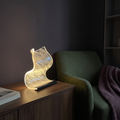 Waveform table lamp glowing on a wooden cabinet beside a green chair